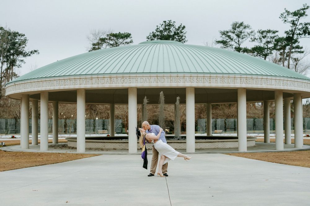 A couple poses under a white gazebo structure with metal roof during their outdoor wedding photoshoot.