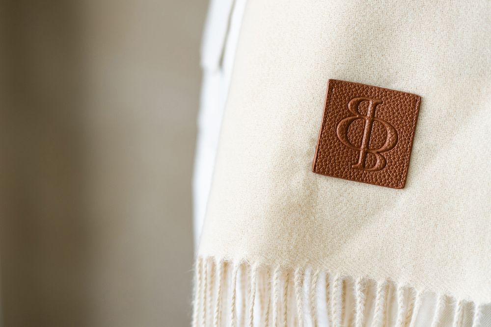 Close-up of brown leather logo tag detail on cream colored fabric showing quality craftsmanship.
