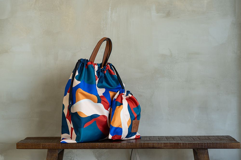 Collection of colorful abstract print handbags displayed on wooden bench against grey wall.