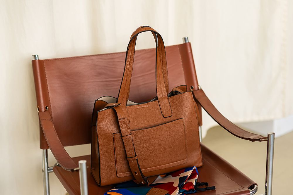 Collection of brown leather messenger bags and totes displayed against beige backdrop.