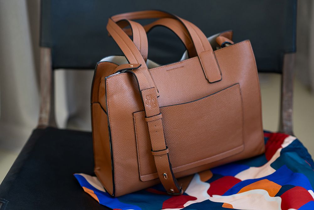 Brown leather duffle bag with buckle details displayed against a blue and red striped background.