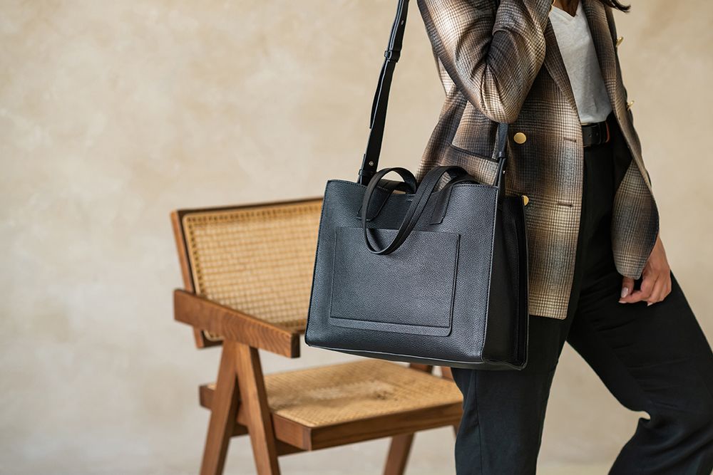 Person in black attire holding a brown leather bag against a light colored wall.