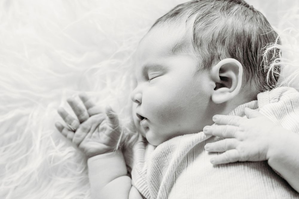 Black and white photo of a peaceful sleeping newborn baby with tiny hands resting near face on soft fur.