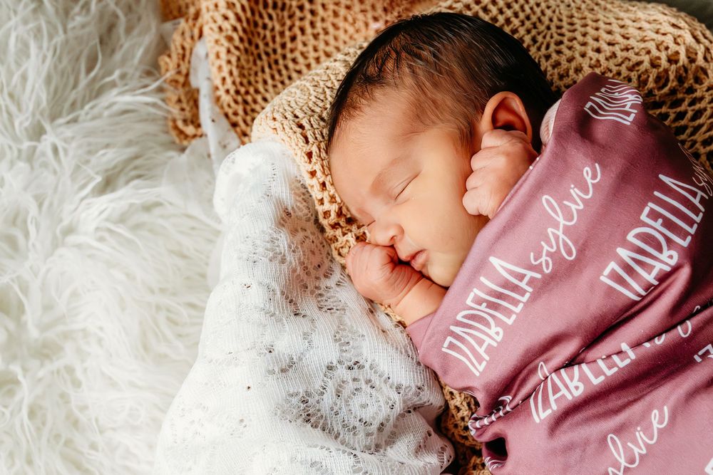 Newborn baby sleeping peacefully wrapped in a personalized pink swaddle blanket with name embroidery.