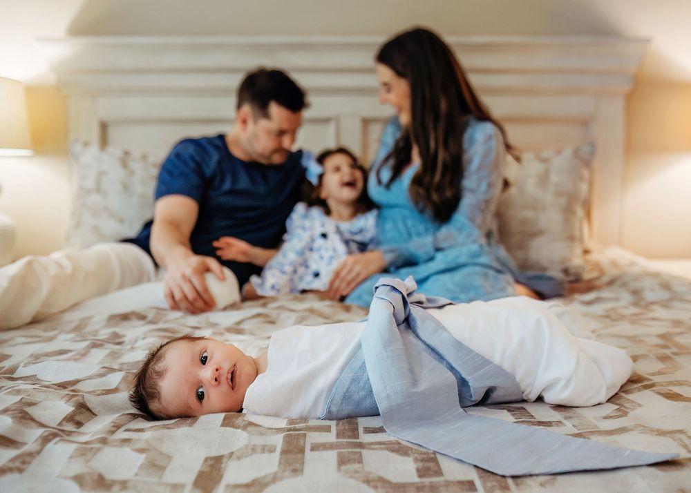 A family photo showing sweet moment between parents and children on a bed with a focus of a newborn during in-home session in Southlake, TX