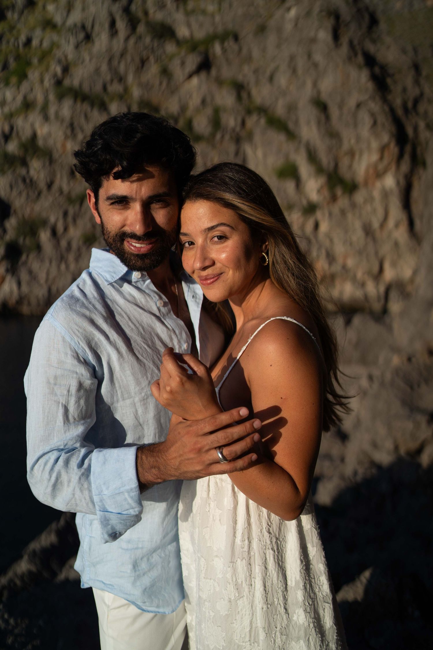 A romantic couple embraces against a rocky backdrop in a series of intimate engagement photos.