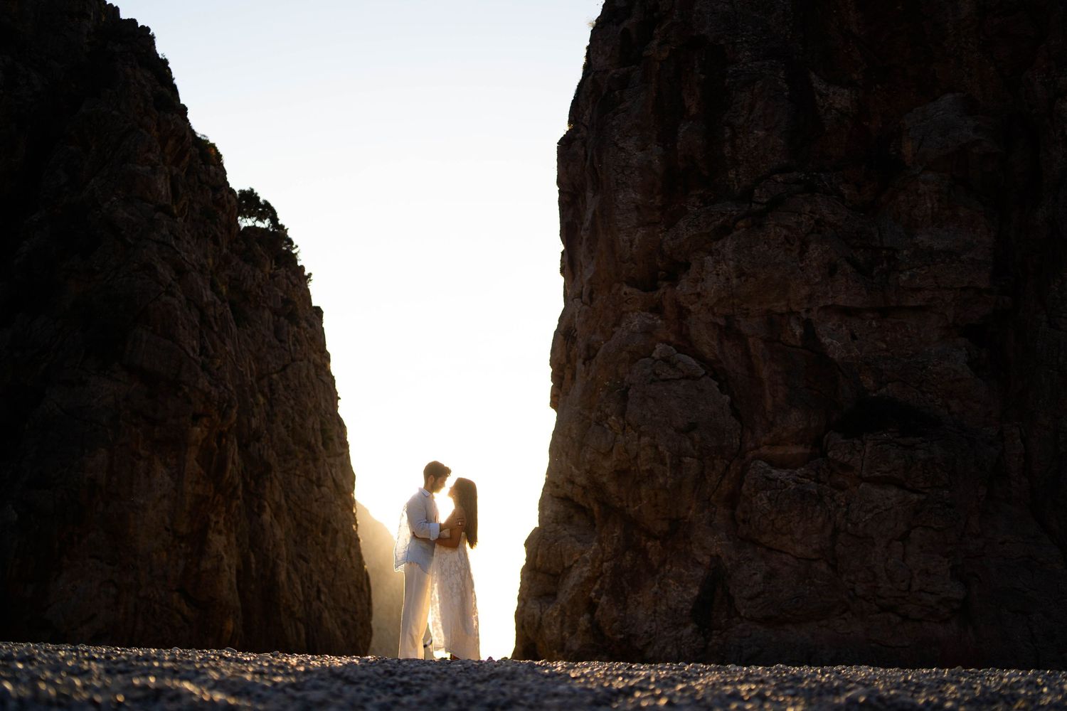 Silhouetted couple standing between towering canyon walls at sunset creating dramatic backlighting effect.