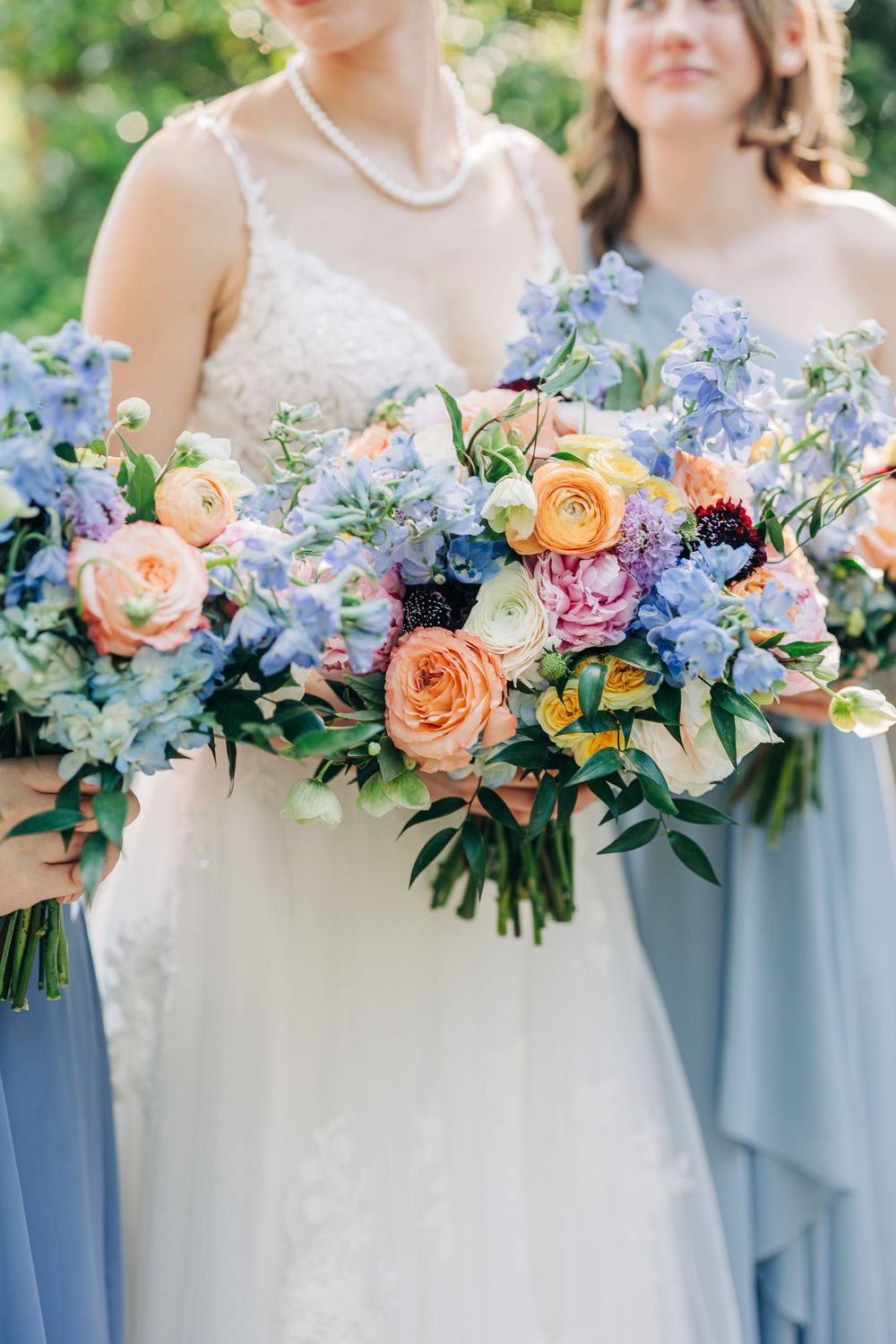 Colorful spring bouquets with blue hydrangeas, peach roses and white flowers against dusty blue dresses at at The Carl House