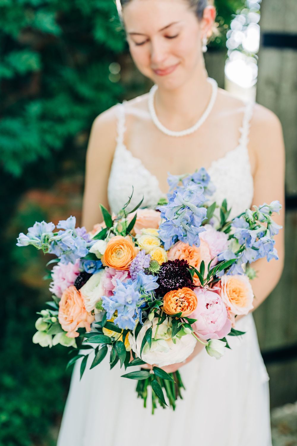 A delicate bridal bouquet features peach roses, blue delphiniums, and dark berries against a soft green background at The Carl House