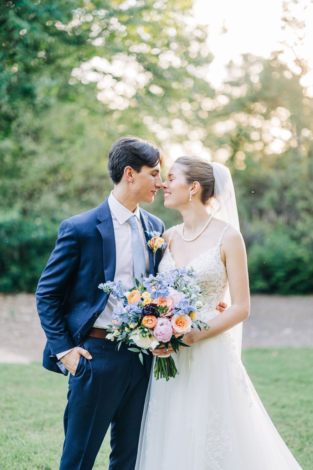 A romantic wedding couple shares tender moments outdoors with a beautiful floral bouquet in soft pastel colors at The Carl House