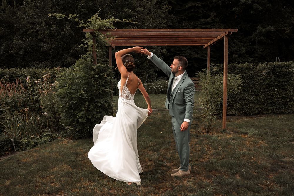A couple dances playfully under a wooden pergola in a garden setting.