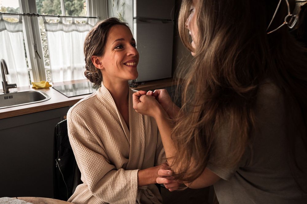 Makeup artist applying cosmetics to a client wearing a beige robe in natural window lighting.
