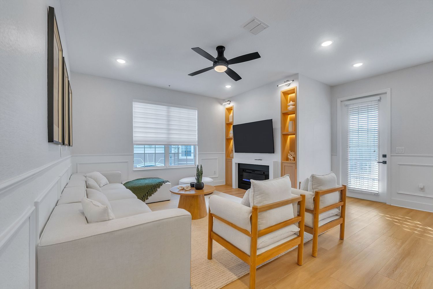 Modern bedroom with hardwood floors, ceiling fan, and large windows showcasing natural light and wooden furniture.