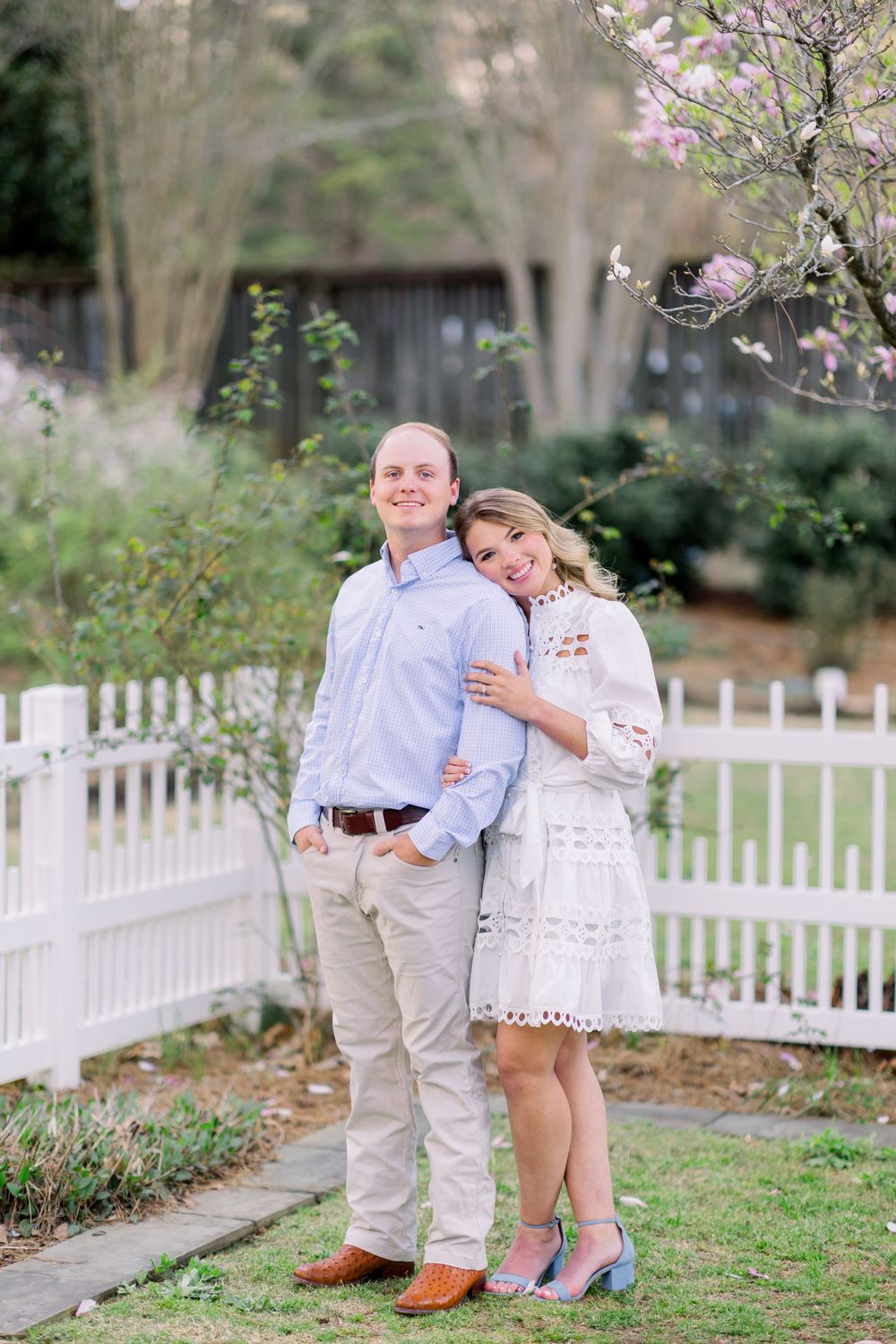 Romantic outdoor photoshoot in a garden with white picket fence and blooming trees.