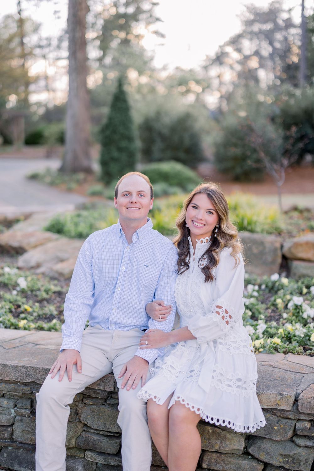Couple sitting on stone wall during outdoor photoshoot in garden setting.