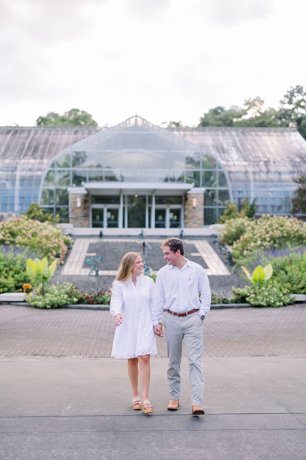 Romantic photoshoot near greenhouse with couple walking on stone pathway.