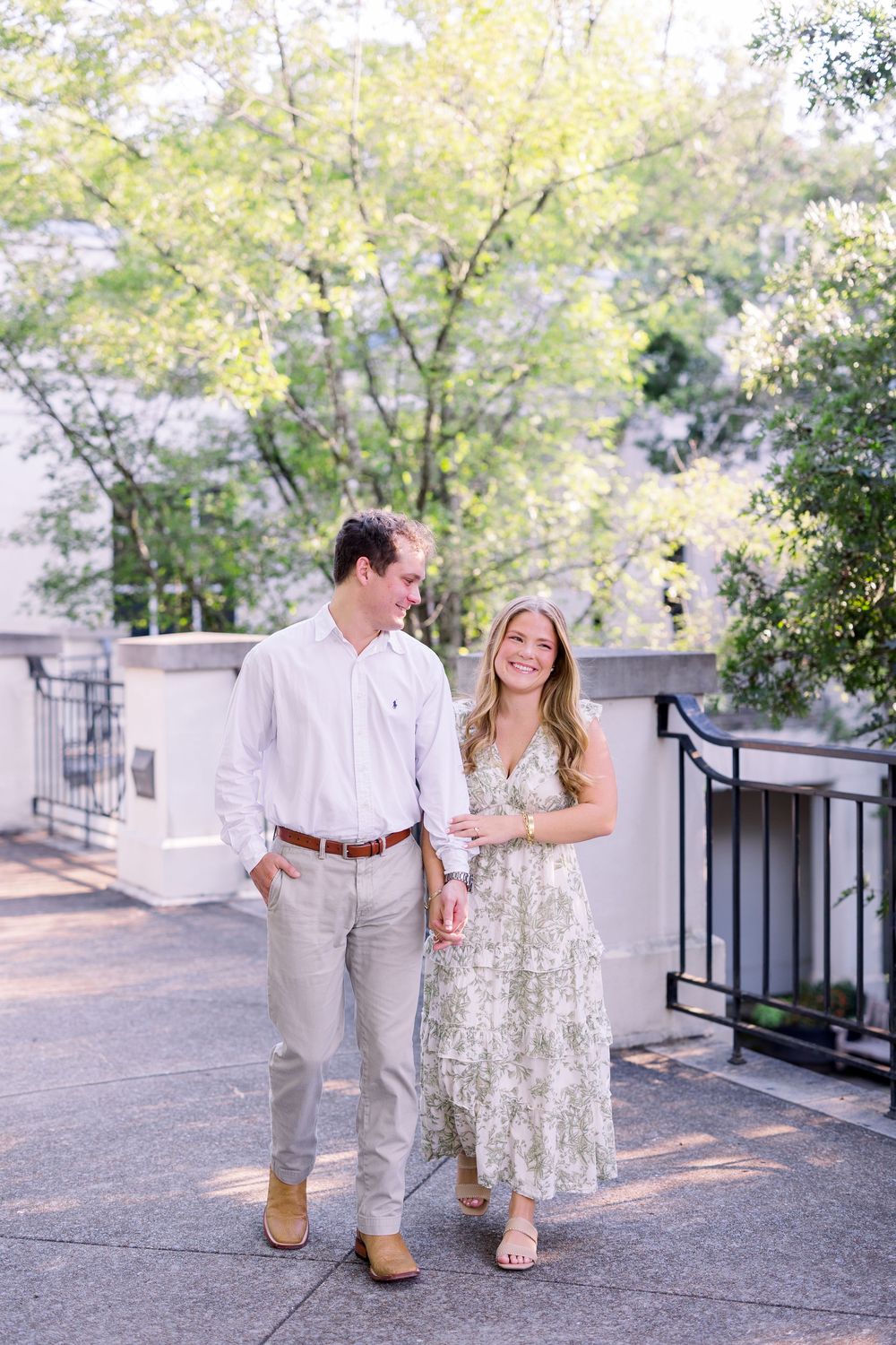 Couple walking together on stone pathway surrounded by trees and white architecture.