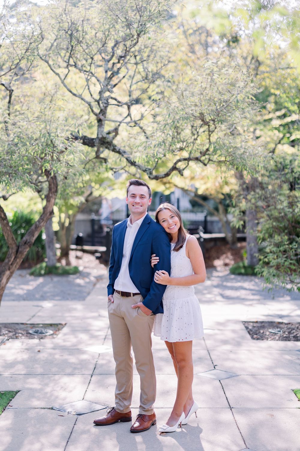 Outdoor engagement session on stone pathway under blooming trees.