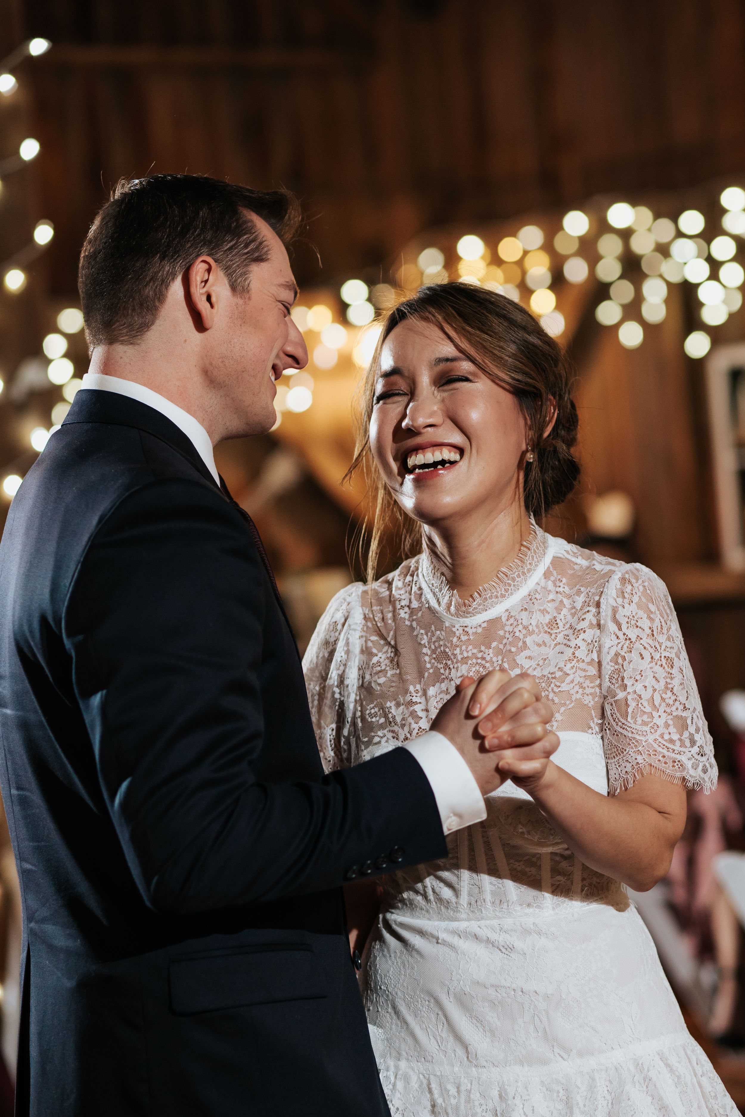 A couple shares a joyful dance moment together at an indoor reception with twinkling lights in the background.
