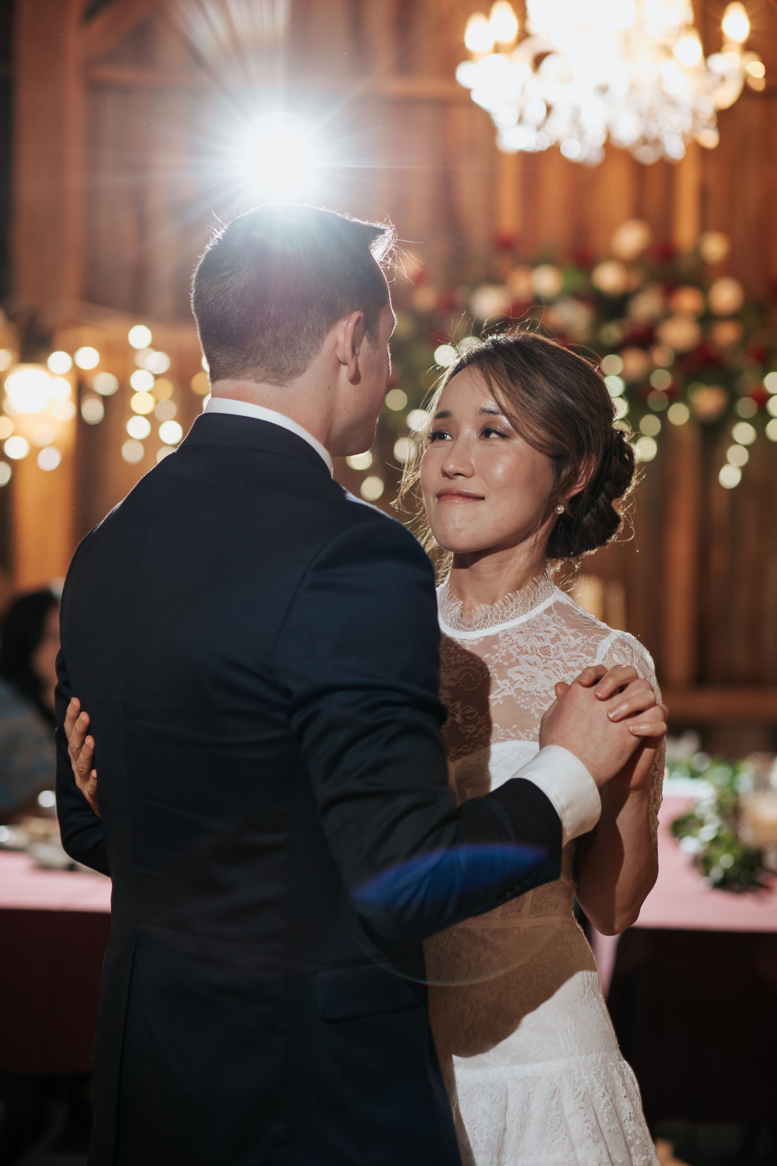 A couple shares an intimate dance at their wedding reception under elegant chandeliers and floral decorations.