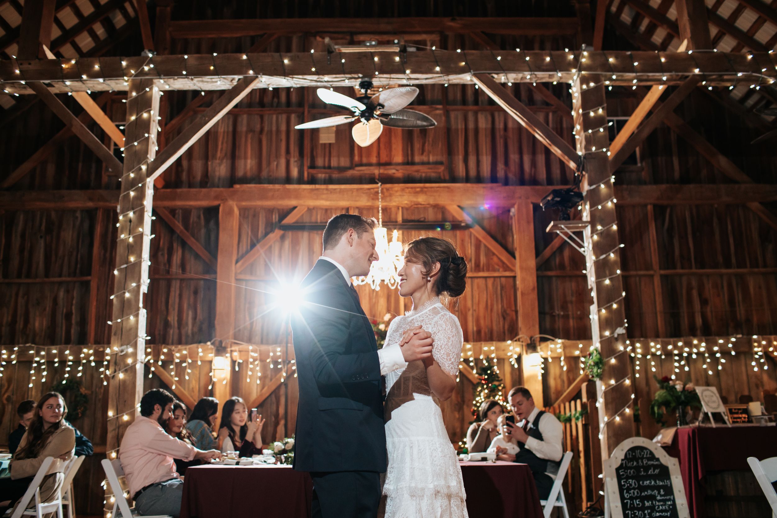 Couples dancing together during a rustic barn wedding reception illuminated by string lights and chandeliers.