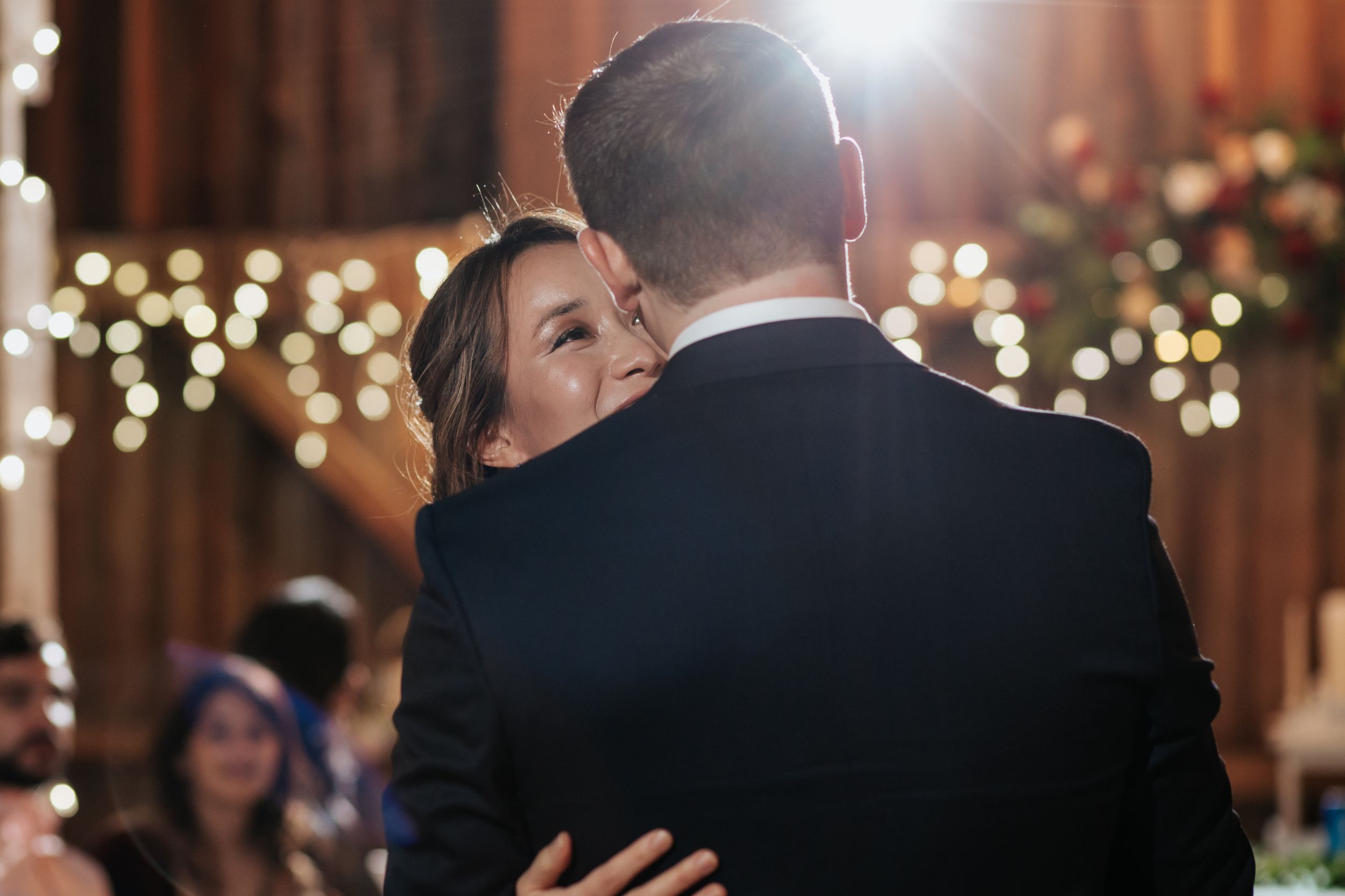 A couple shares an intimate dance moment at their wedding reception with twinkling lights in the background.
