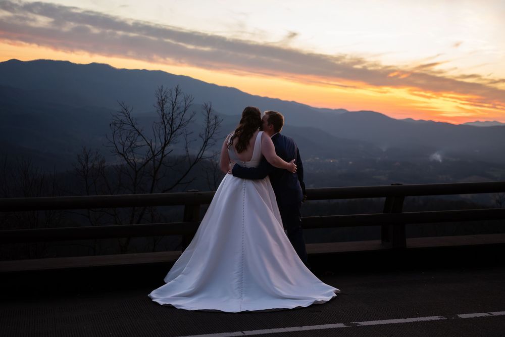 Silhouettes of a couple in wedding attire embrace against a dramatic mountain sunset backdrop.