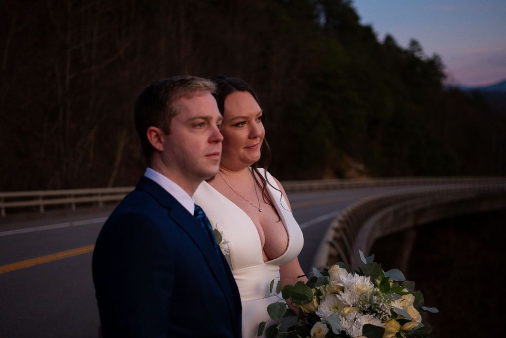 Wedding couple shares intimate moment on mountain road at dusk.