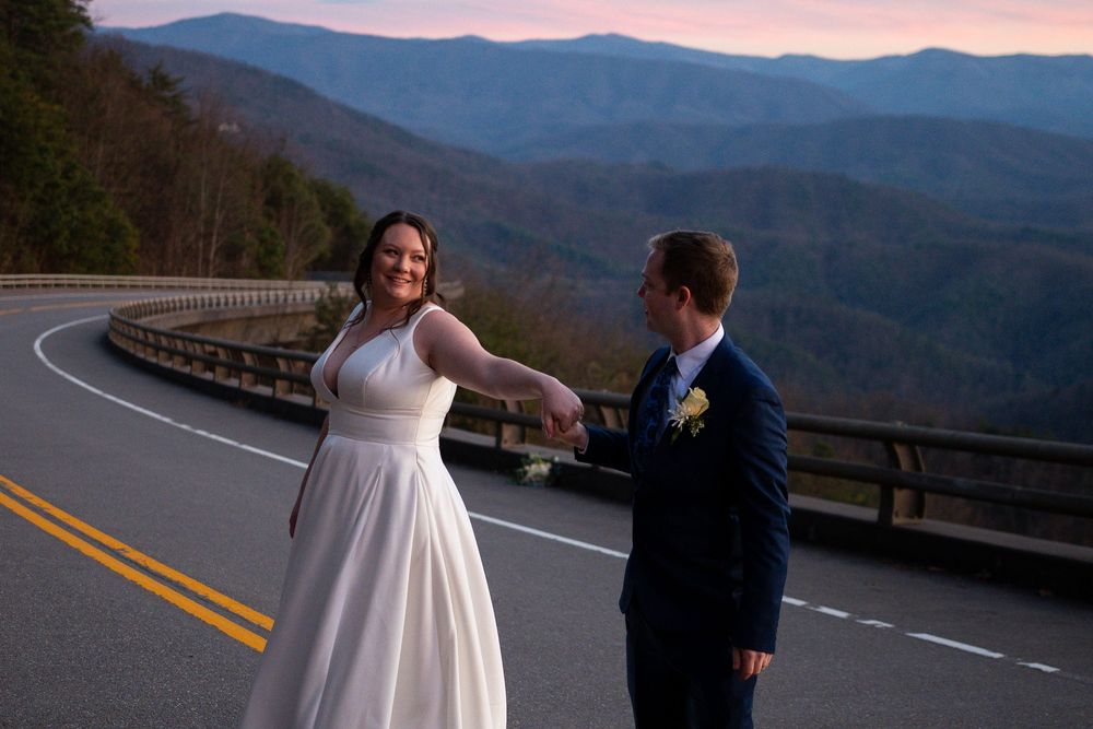 A romantic moment shared on a mountain road during sunset with rolling hills in the background.