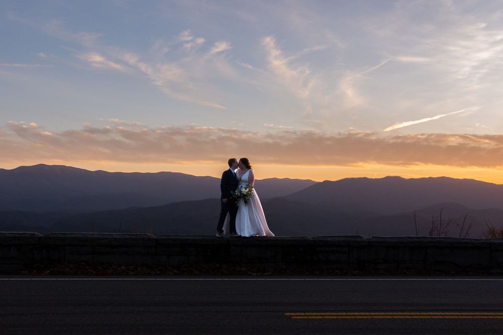 Silhouettes of a couple embrace against a dramatic mountain sunset creating a romantic panoramic view.
