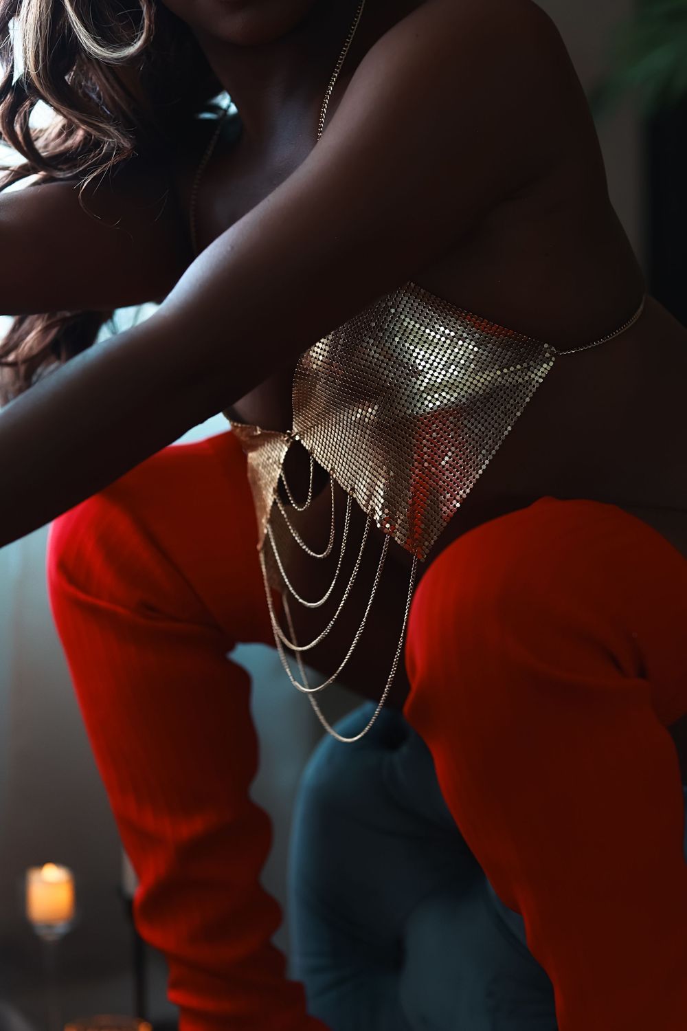 A figure in a bright red sweater and metallic mesh face covering poses dramatically in a dark setting.