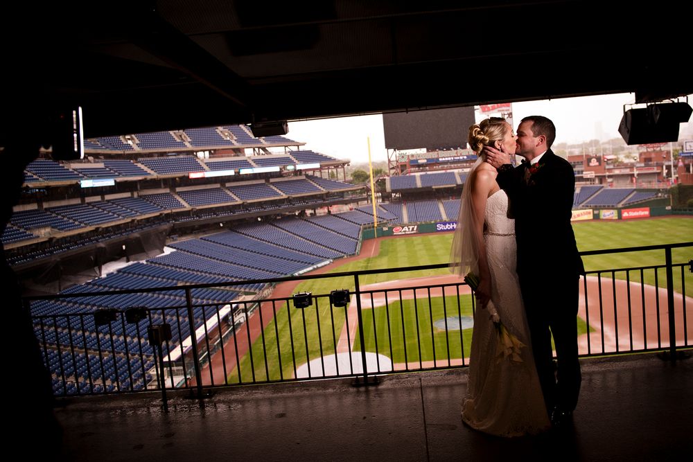 A couple embraces in silhouette against a sunlit baseball stadium backdrop during a romantic photo session.