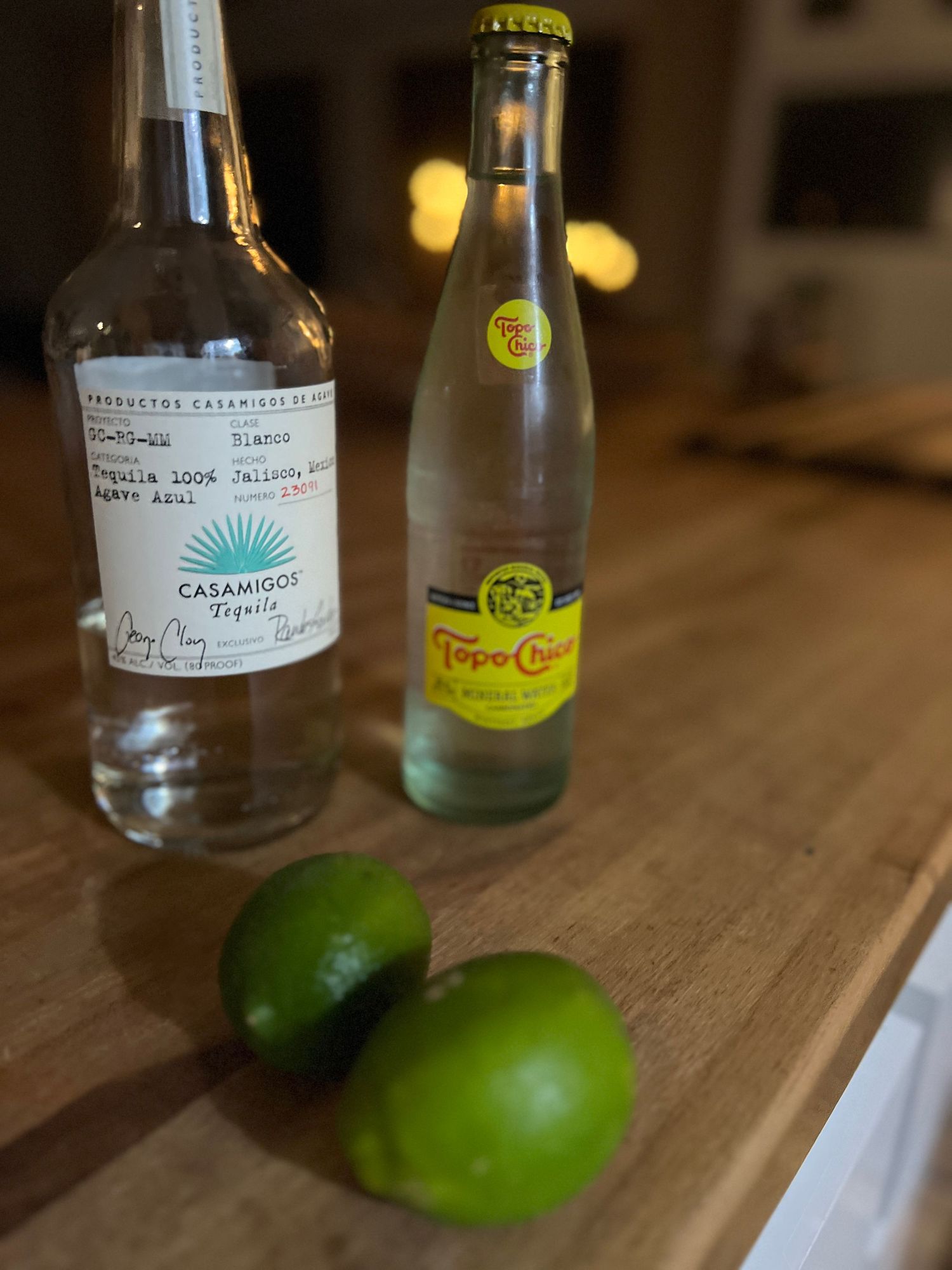 Glass bottles and a fresh lime sit on a wooden surface in moody lighting.