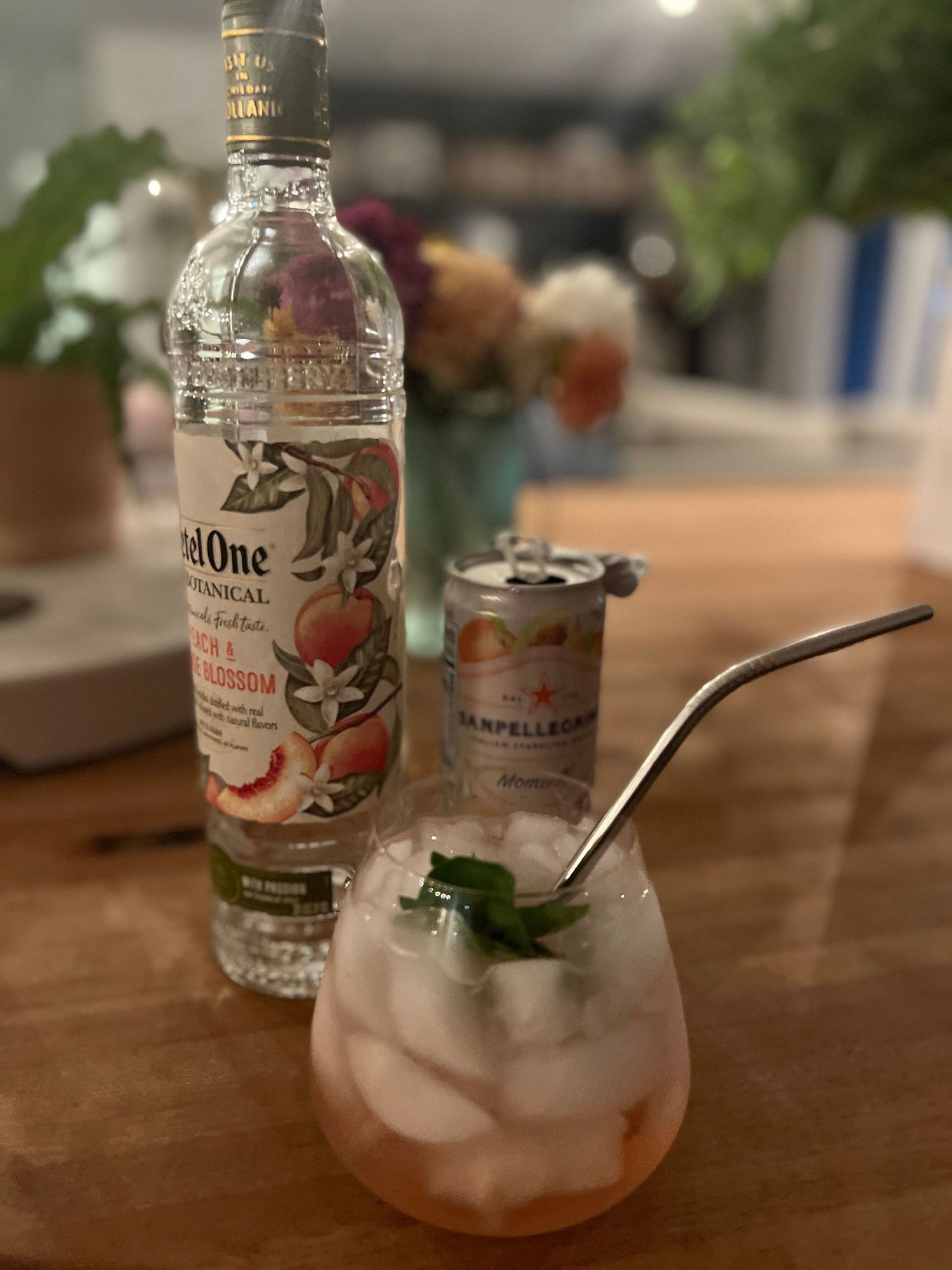 A cocktail glass with ice and garnish sits next to a bottle of Ketel One vodka and mixer on a wooden table.