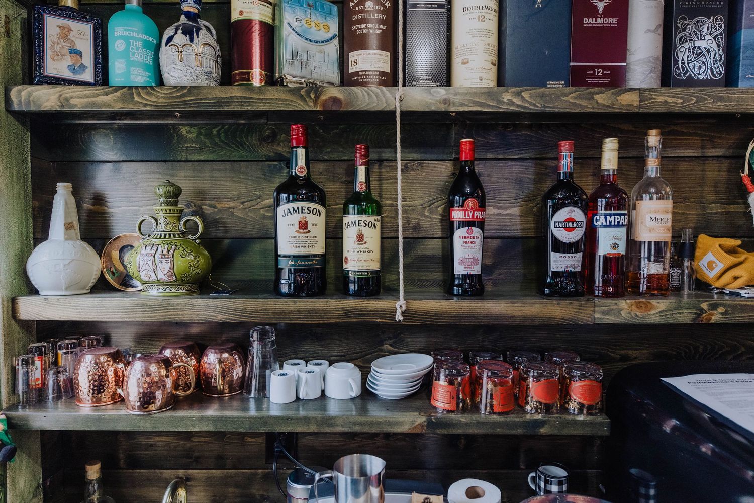 A well-stocked bar shelf displays various liquor bottles, glassware, and bar accessories in warm lighting.