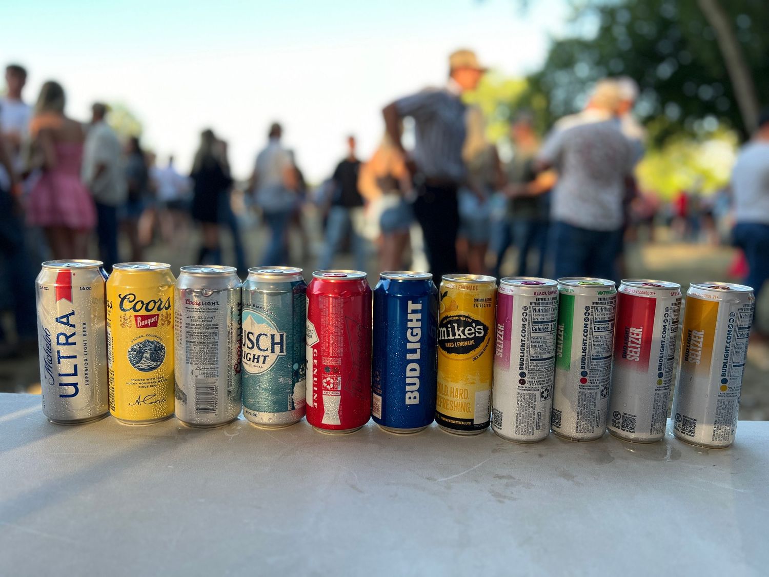 A lineup of various beer cans arranged in a row on a wooden surface with blurred background.