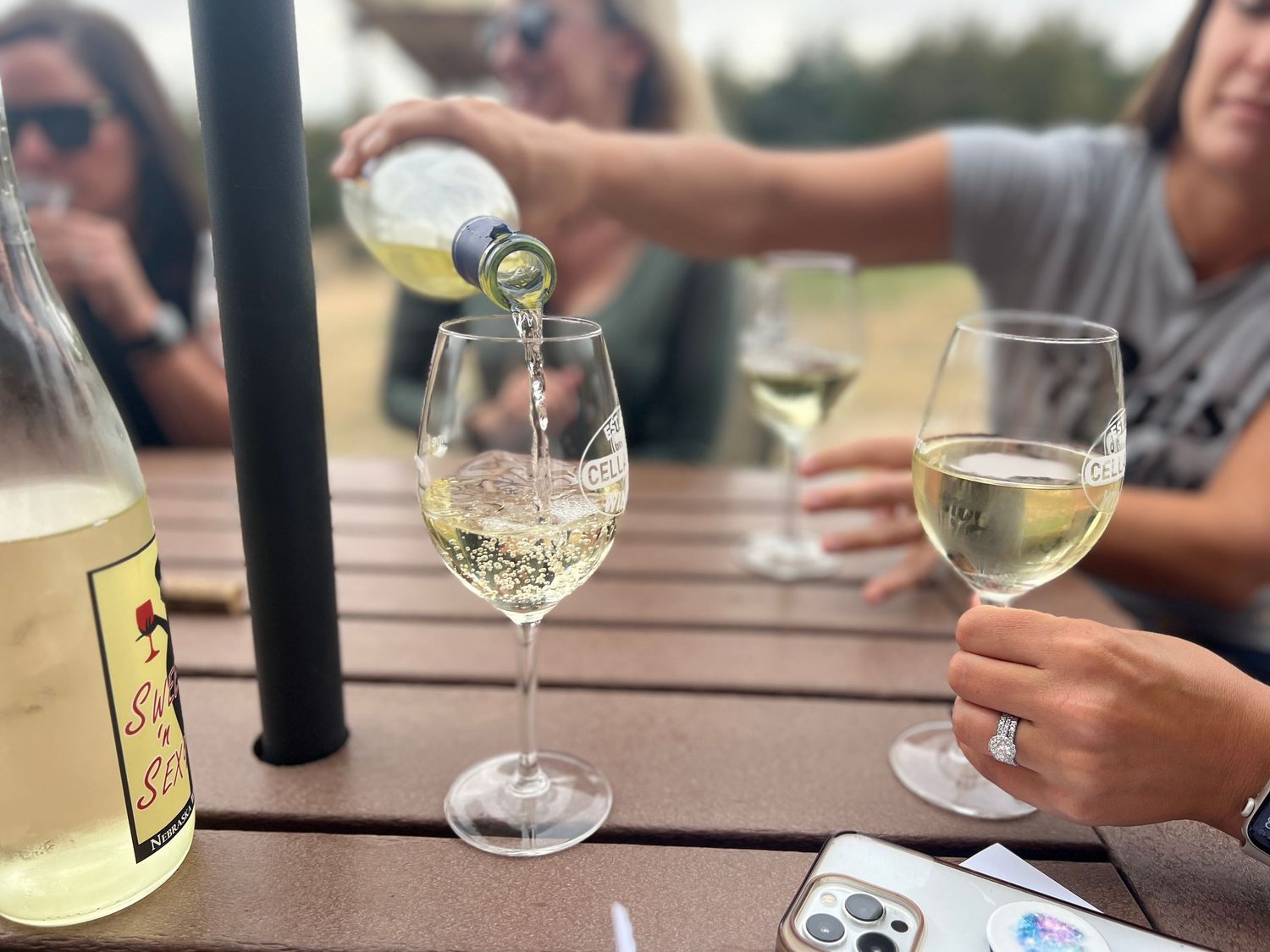 People enjoying glasses of white wine at an outdoor table during a sunny day.