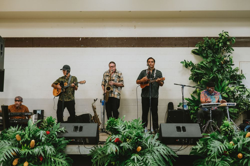 Band performing on stage with tropical plants and foliage decorations.