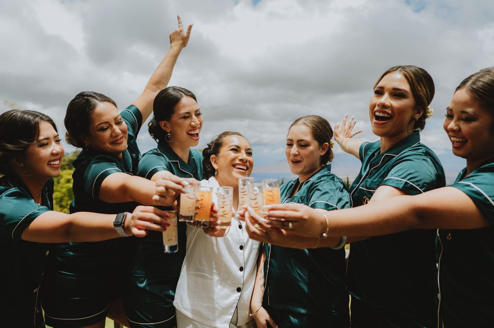 Bridesmaids in teal dresses share celebratory drinks and laughter during a wedding celebration.