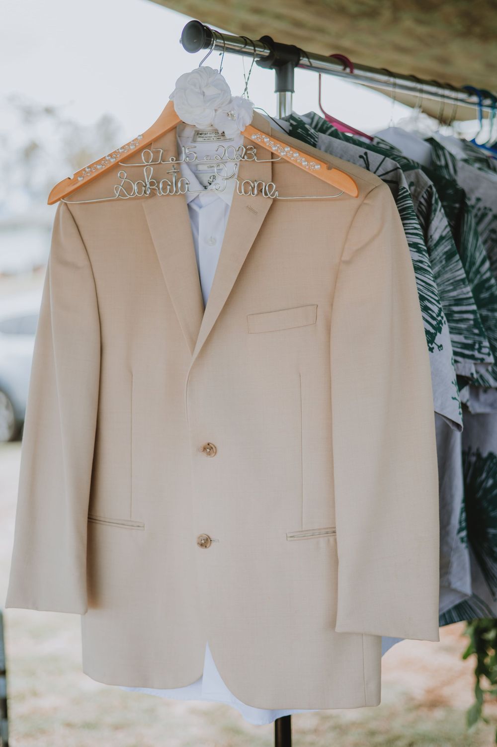 Cream colored suit jackets hanging on personalized wooden hangers against a light background.