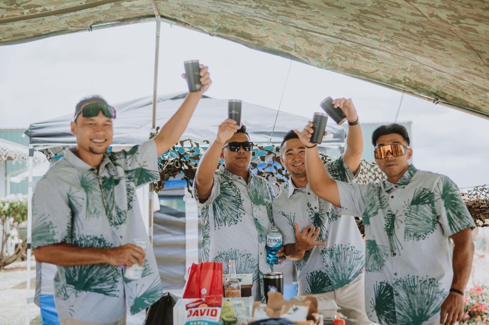 Wedding party in tropical print shirts takes photos with their phones outdoors.
