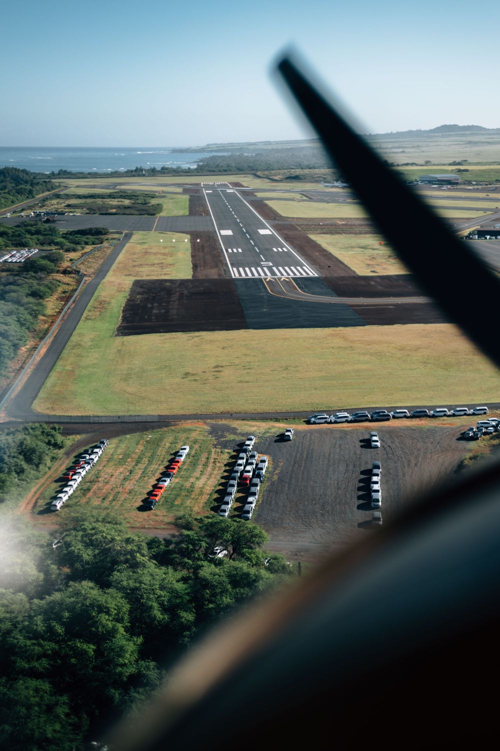 Aerial view of a rural airport runway with parked vehicles visible from above.