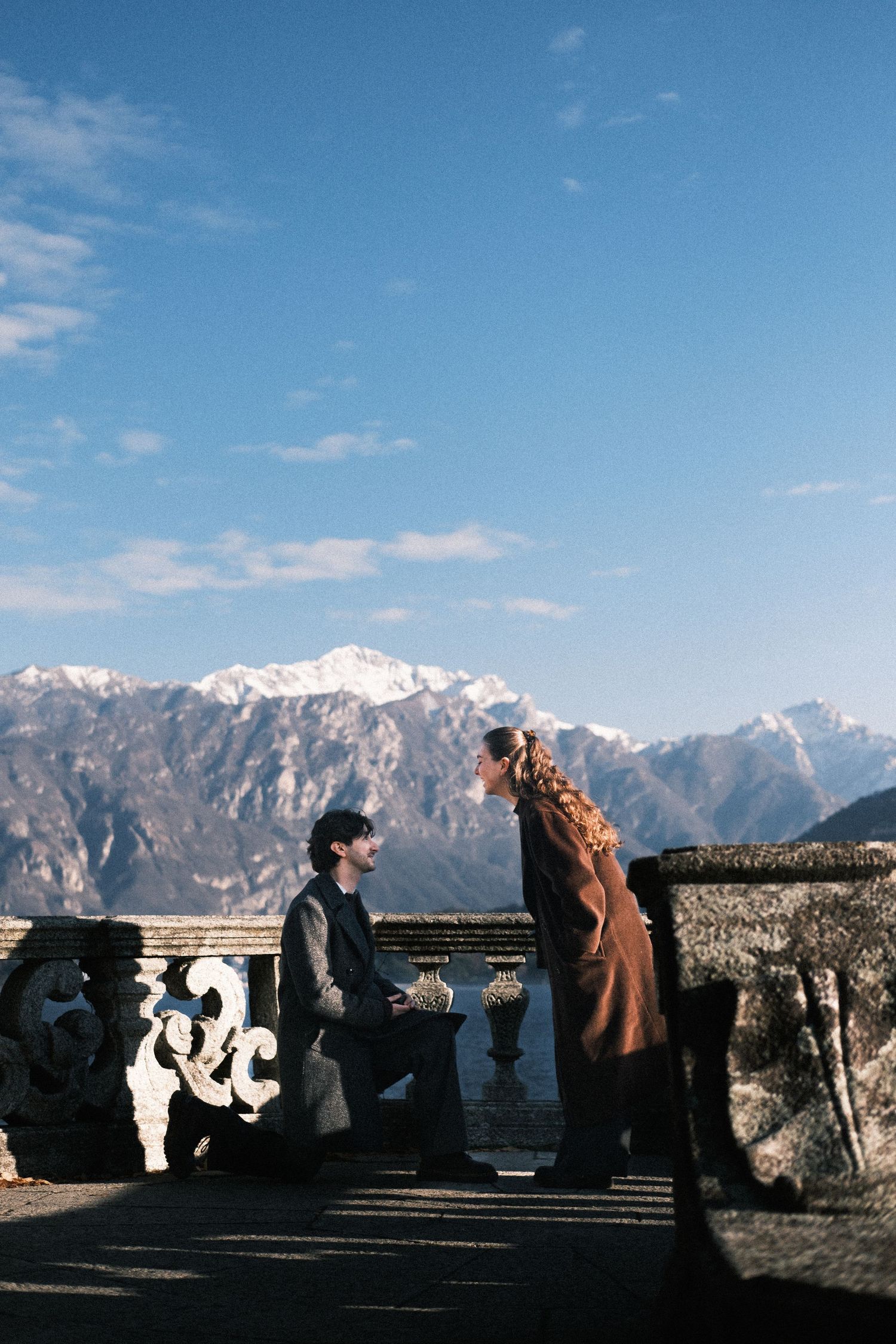 A panoramic view of snow-capped mountains and stone balustrades against a bright blue sky with scattered clouds.