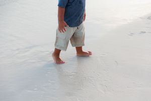 Bare feet walking on wet sand at the beach leaving footprints in the shallow water.