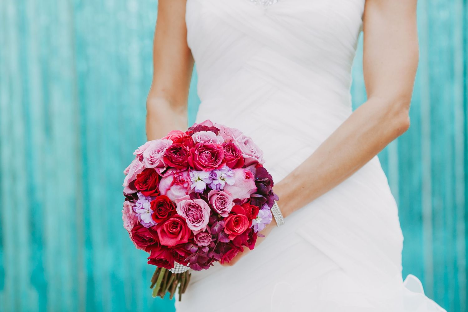 Pink and red rose wedding bouquets against a turquoise blue background showcase vibrant floral arrangements.