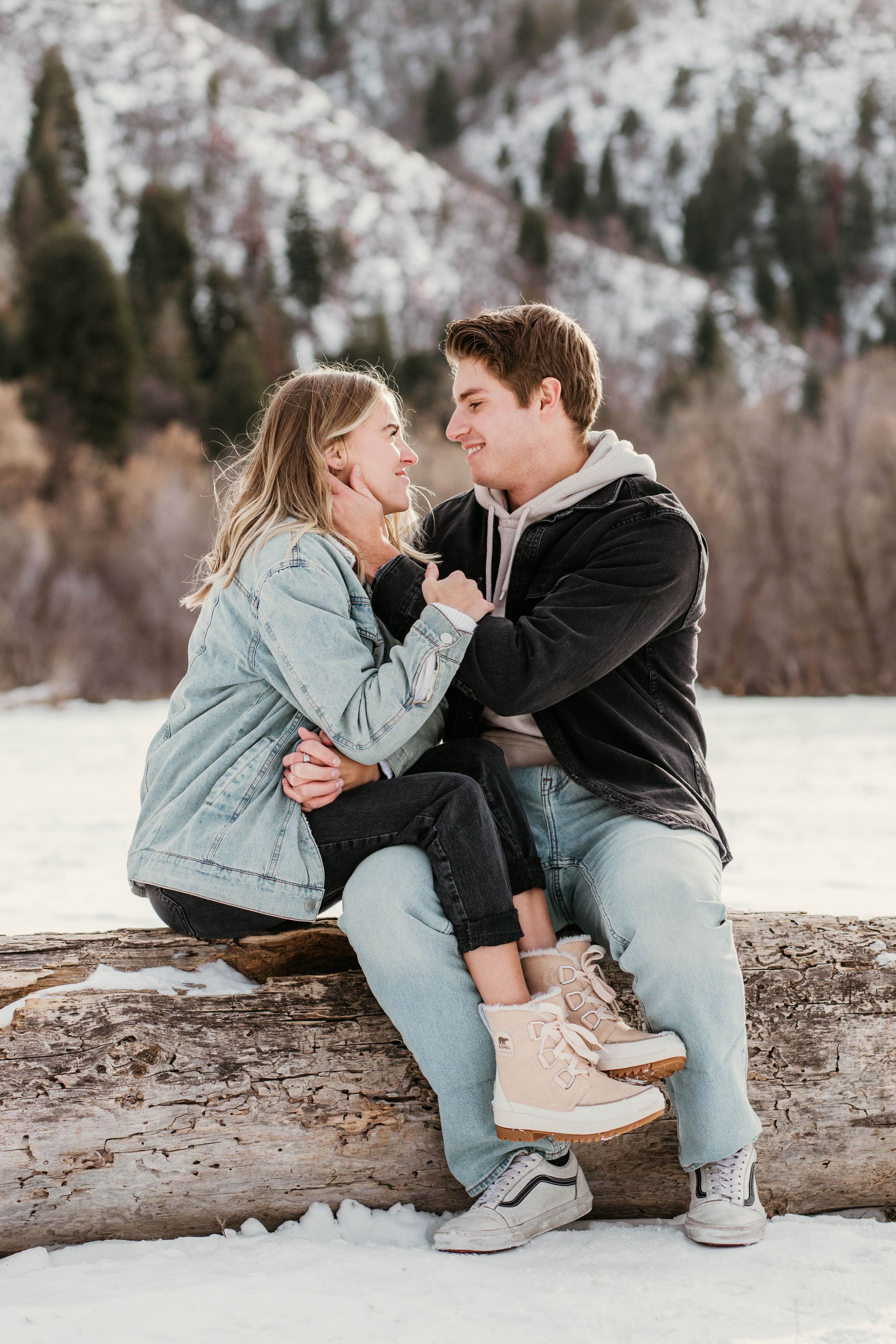 A couple sits together on a snowy log sharing intimate moments in winter scenery.