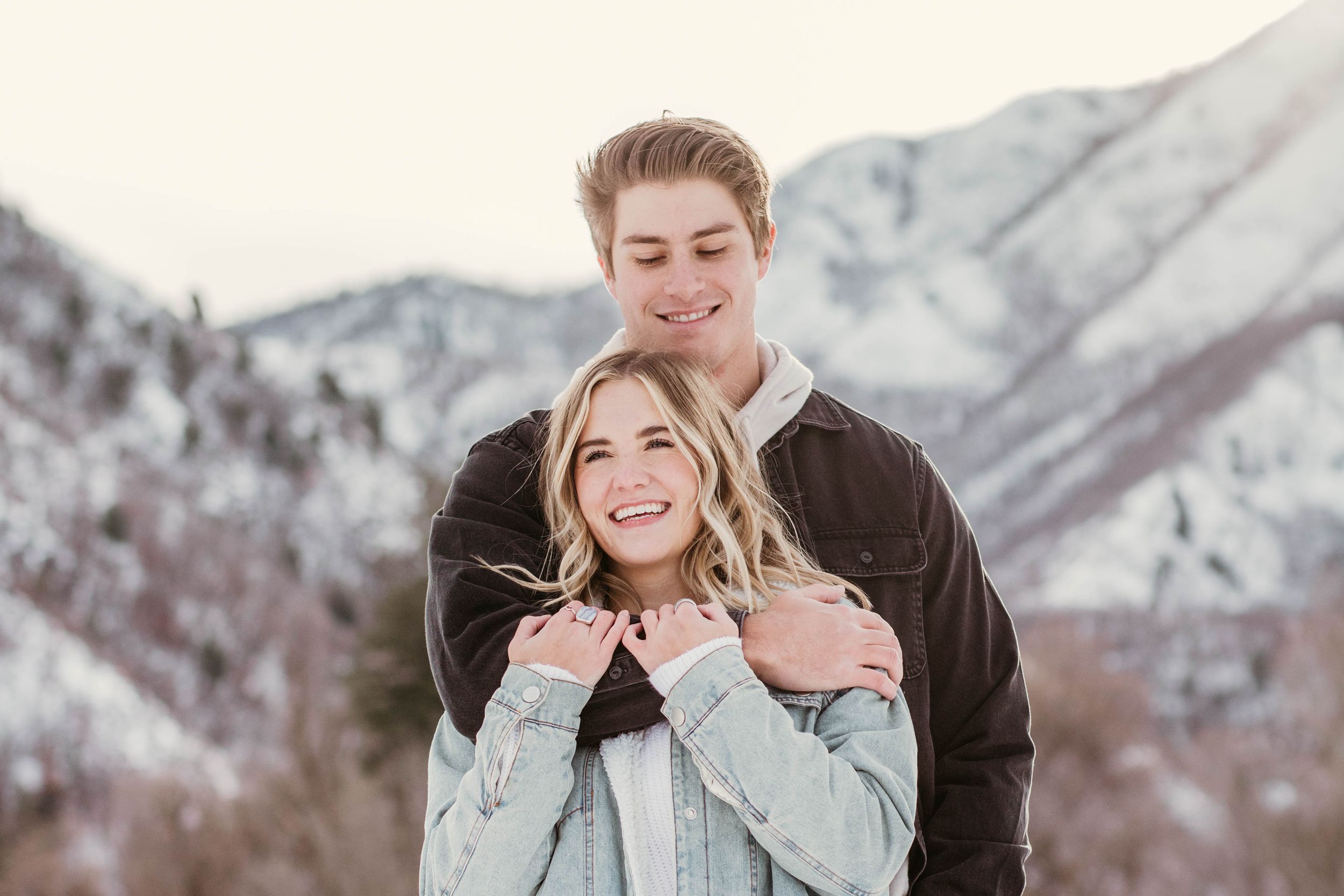 A couple shares joyful moments together against a snowy mountain backdrop during a winter photo session.