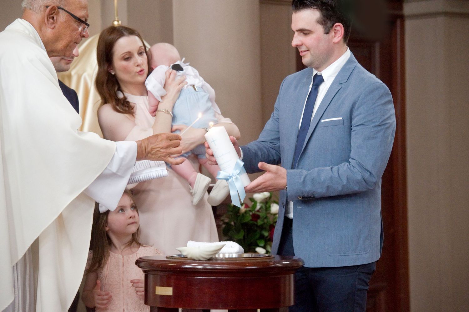 Religious ceremony with family and clergy gathered around baptismal font.