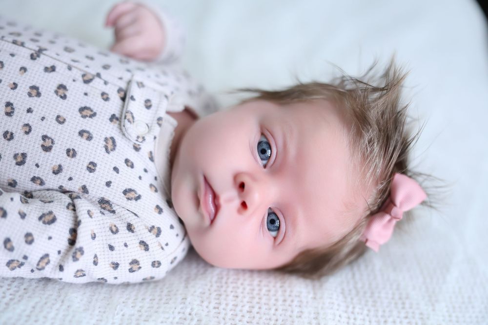 Baby lying on white bedding looking at camera.
