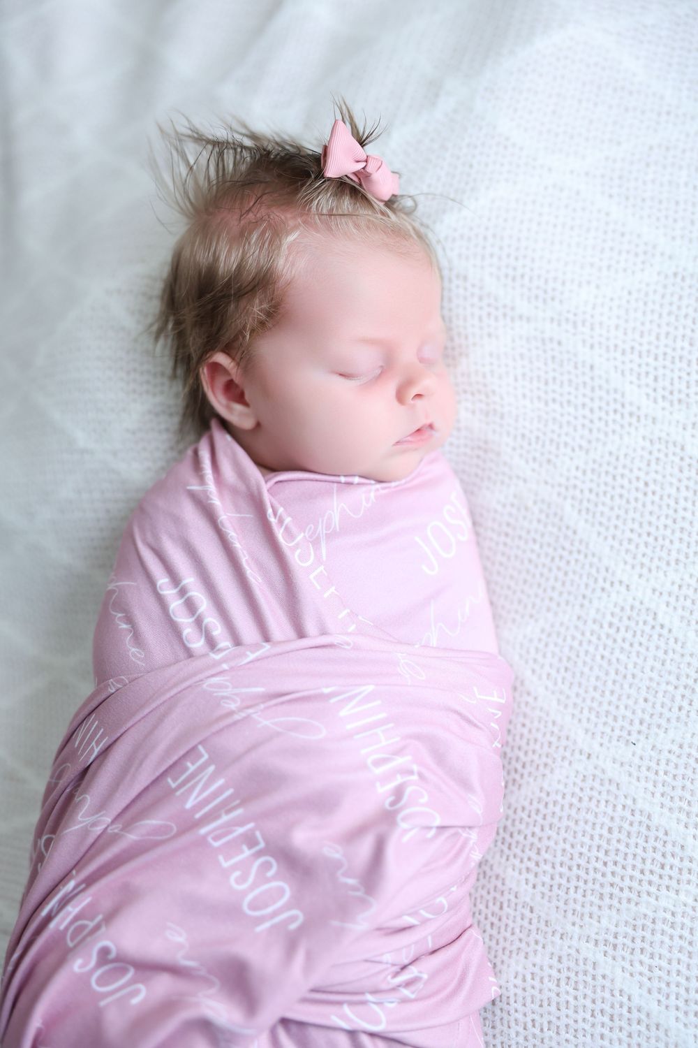 Sleeping newborn wrapped in pink swaddle blanket on white blanket.